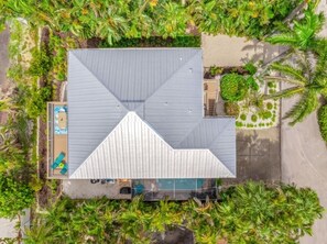 An aerial view of a modern building with a unique triangular roof design, surrounded by lush greenery and a swimming pool.