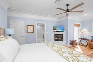 A bedroom with a bed, a ceiling fan, a fireplace, a TV, and a door. - Anchored Here 3 Bedroom Home by RedAwning (Captiva)