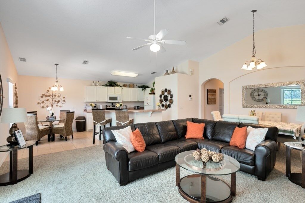 A modern living room with a black leather sofa, a glass coffee table, and a dining area with wicker chairs.