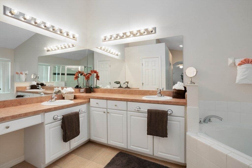A modern bathroom with two sinks, vanity cabinets, a large mirror, and a bathtub.