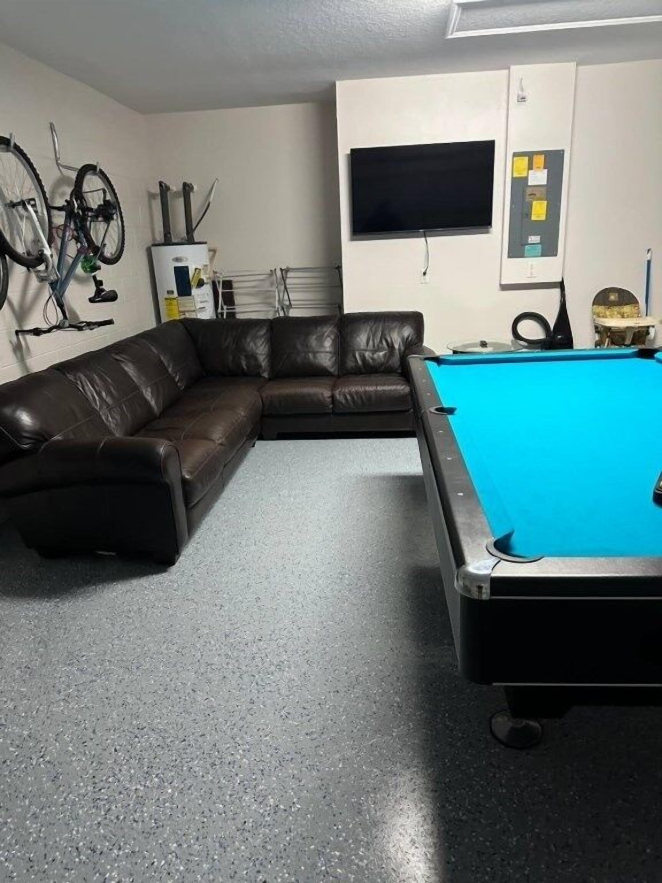 A room with a pool table, a leather sofa, a TV mounted on the wall, and exercise equipment.