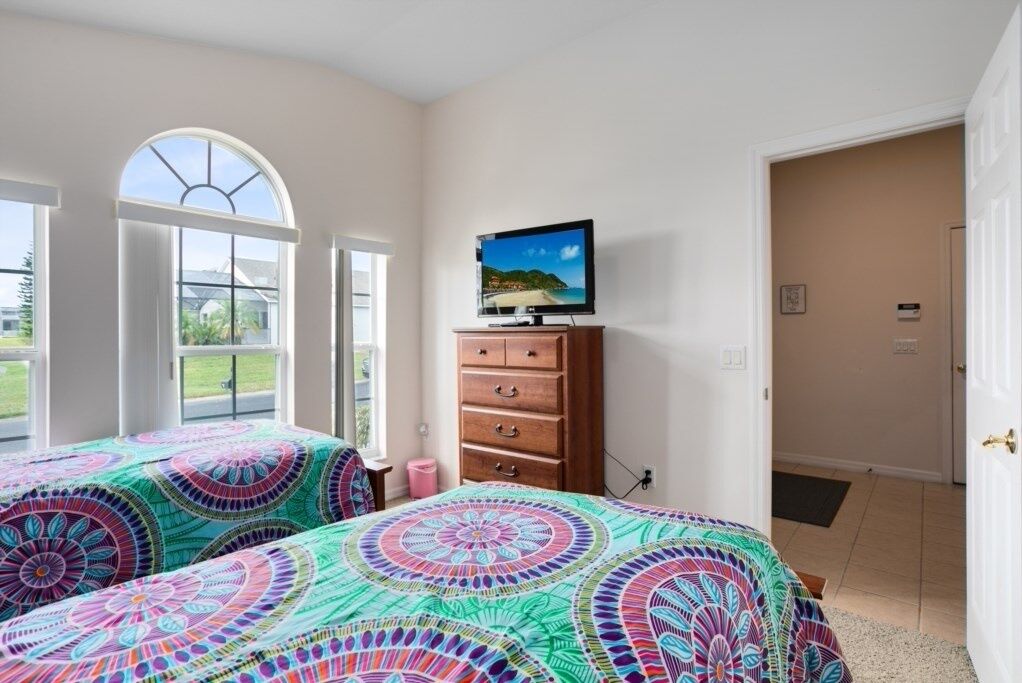 A bedroom with two beds, a TV on a dresser, and large windows with a view of the outdoors.