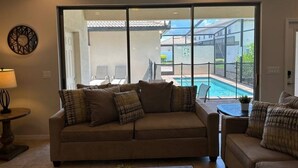 A living room with a beige sofa, a coffee table, and a view of a swimming pool through large glass doors. - Lovely 5br Townhouse At Windsor At Westside 5 Bedroom Townhouse by RedAwning (Kissimmee)