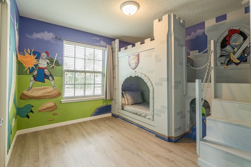 Habitación infantil con mural de castillo, una ventana con persianas y una cama con cabecera estilo castillo.