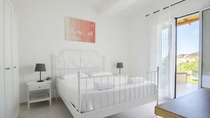 A white bedroom with a bed, nightstands, a table, and a view of the outdoors. - TWO ROOMS SEA VIEW APARTMENT (FORIO)