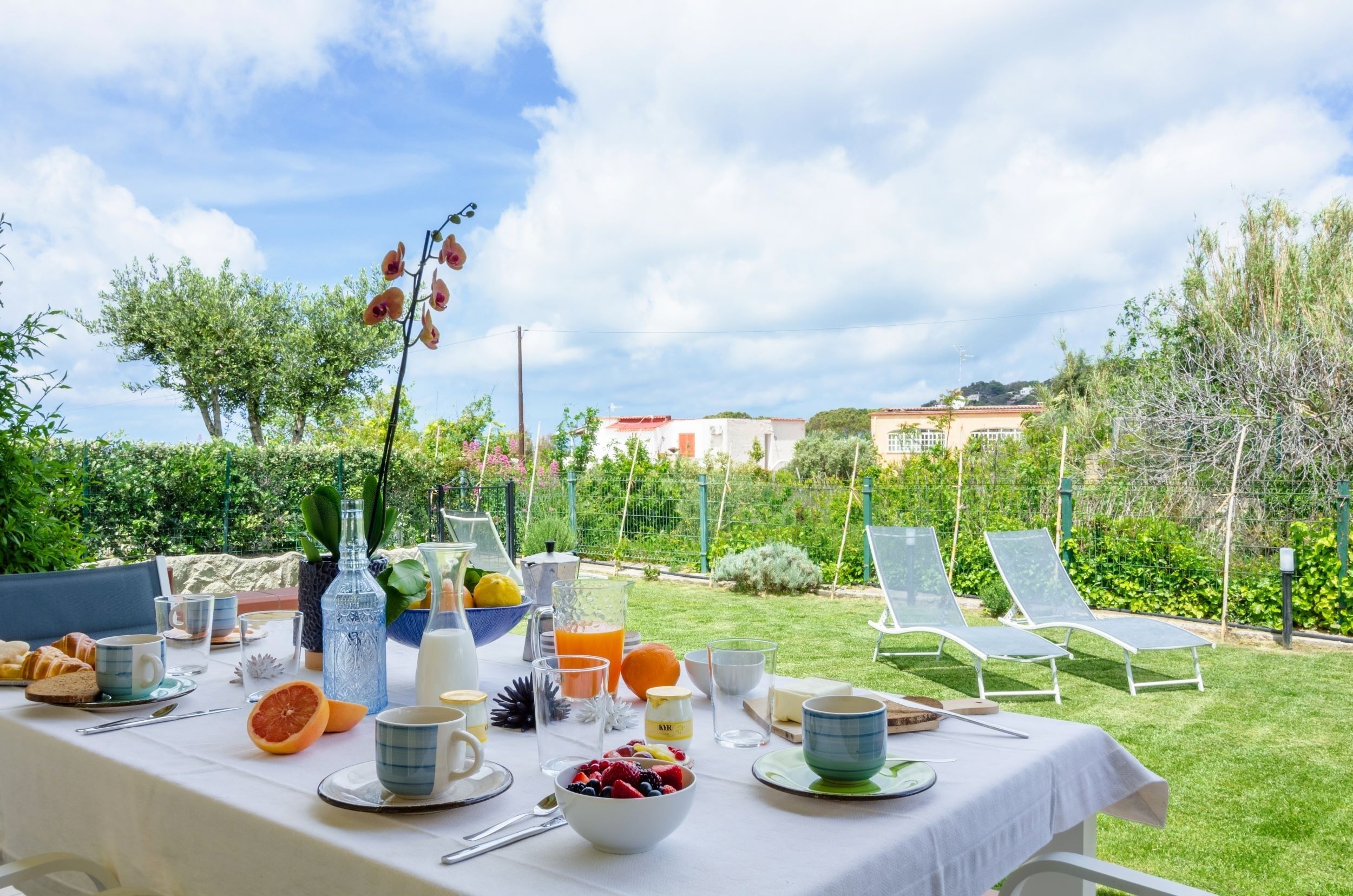 An outdoor breakfast setup with a table, chairs, and a garden view.