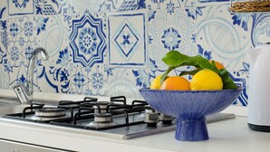 A kitchen with a gas stove, a blue bowl with fruits, and blue patterned tiles. - TWO ROOMS SEA VIEW APARTMENT (FORIO)