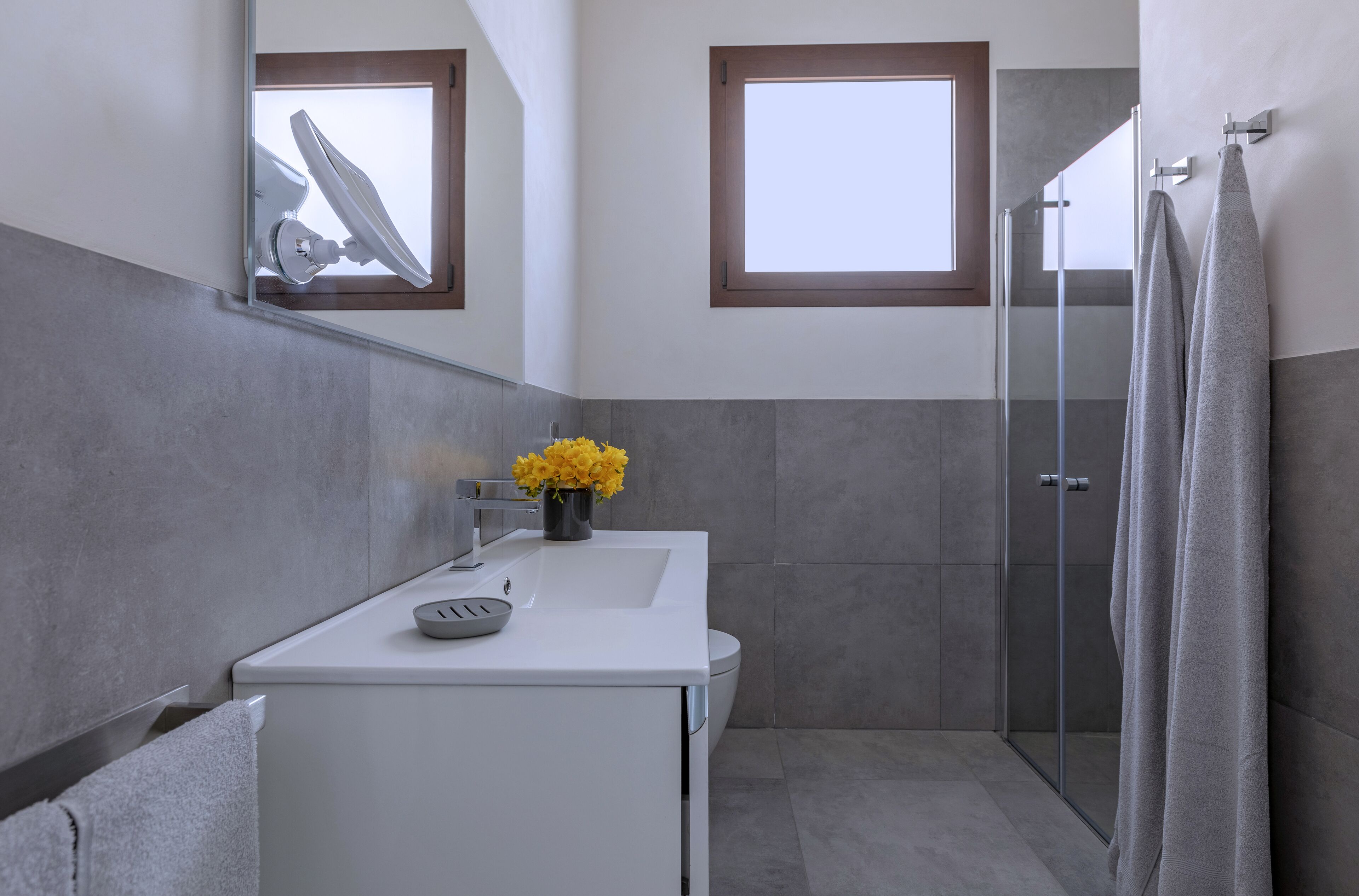 Ein modernes Badezimmer mit einem weißen Waschbecken, einer Duschkabine aus Glas und einem Fenster für natürliches Licht.