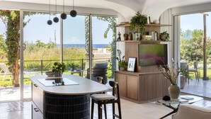 Une cuisine moderne dotée d’un îlot central, d’un coin repas avec une table en marbre et d’une grande fenêtre offrant une vue sur l’extérieur.