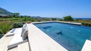 Une piscine d’un bleu éclatant, dotée de chaises longues et offrant une vue sur la mer et les montagnes.