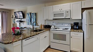 A kitchen with white cabinets, a granite countertop, a microwave, a stove, and a refrigerator. - Grand Beach Resort #311 - Close to Beach with Gulf Views and Resort Amenities (Gulf Shores)