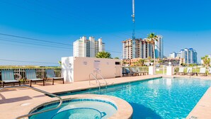 A swimming pool with lounge chairs and a hot tub, surrounded by tall buildings. - Grand Beach Resort #311 - Close to Beach with Gulf Views and Resort Amenities (Gulf Shores)