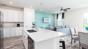 A modern kitchen with white cabinets, a large island, and a dining area with a blue sofa and chairs. - Margaritaville Fun in the Sun - Townhome (Kissimmee)