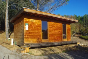 A wooden cabin with a door and a window, surrounded by trees.