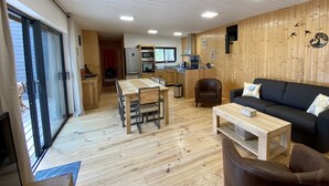 Een ruime woonkamer met een houten vloer, een eettafel, een bank en een keuken op de achtergrond.