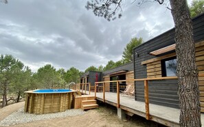 Eine Holzhütte mit einer Sonnenterrasse, einem Whirlpool und Blick auf den umliegenden Wald.