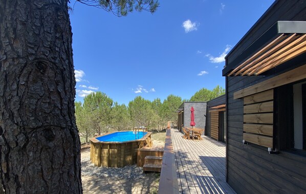 A wooden deck with a hot tub, a small table and chairs, and a wooden building with a red umbrella.