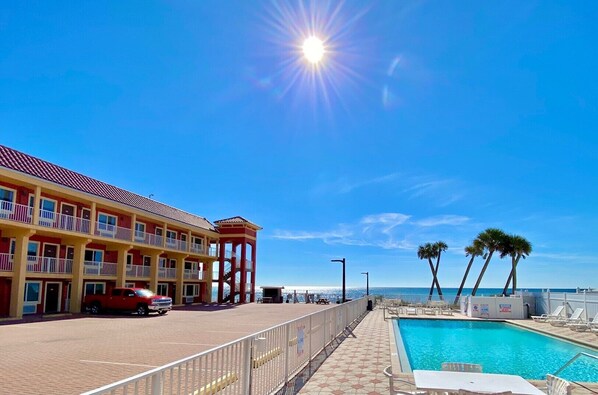 A hotel with a pool, a red car, and a clear blue sky.