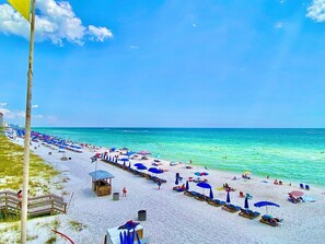 A beach with rows of sun loungers and umbrellas, a lifeguard tower, and a clear view of the ocean.