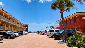 Un hotel de fachada roja, con varios balcones y un estacionamiento con varios coches.