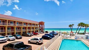 Hotel con piscina, vista al mar y estacionamiento lleno de coches.