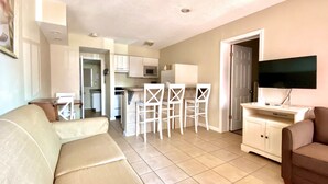 Un espacio habitable compacto con sofá, televisor, pequeña cocina y comedor.