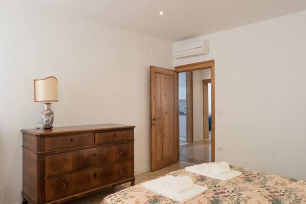 Un dormitorio con un aparador de madera, una cama con ropa de cama floral y una puerta abierta que da a otra habitación.
