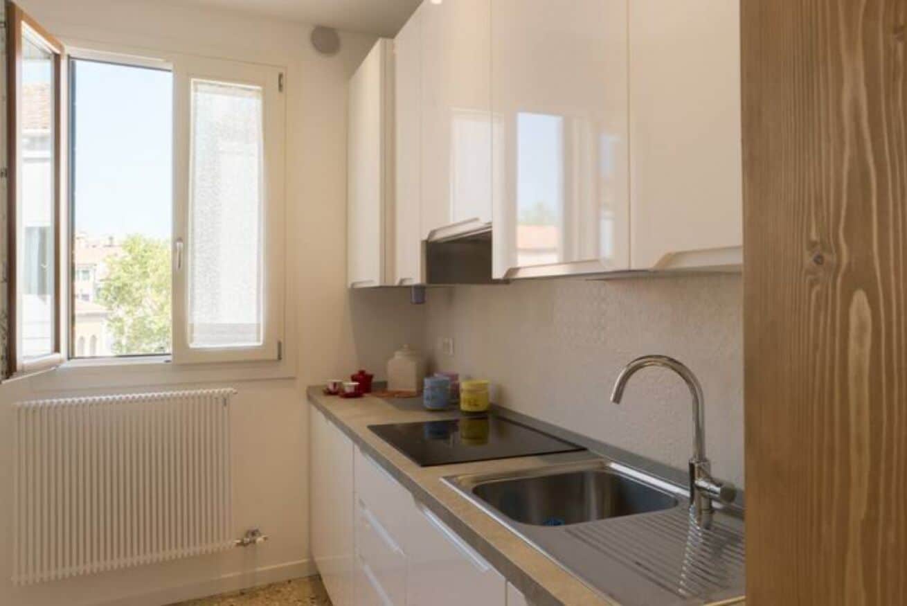 A kitchen with a window, white cabinets, a sink, and a radiator.
