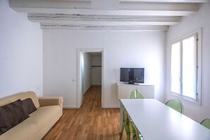 A room with a sofa, a dining table, chairs, a television on a stand, and a window. - Rialto al Manganer, apartment near Rialto Mercato (Venezia)