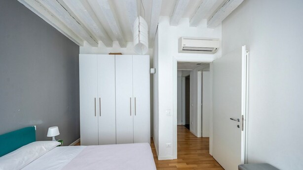 A bedroom with a bed, a wardrobe, an air conditioning unit, and a hallway leading to another room.