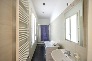 A narrow bathroom with a white radiator, a large mirror, and a white sink.