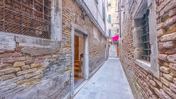 Un stretto vicolo con pareti in pietra e pavimento piastrellato, che conduce a un edificio con porta aperta.
