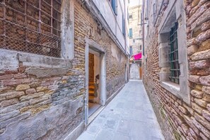 A narrow alleyway with stone walls and a tiled floor, leading to a building with an open door. - Rialto al Manganer, apartment near Rialto Mercato (Venezia)