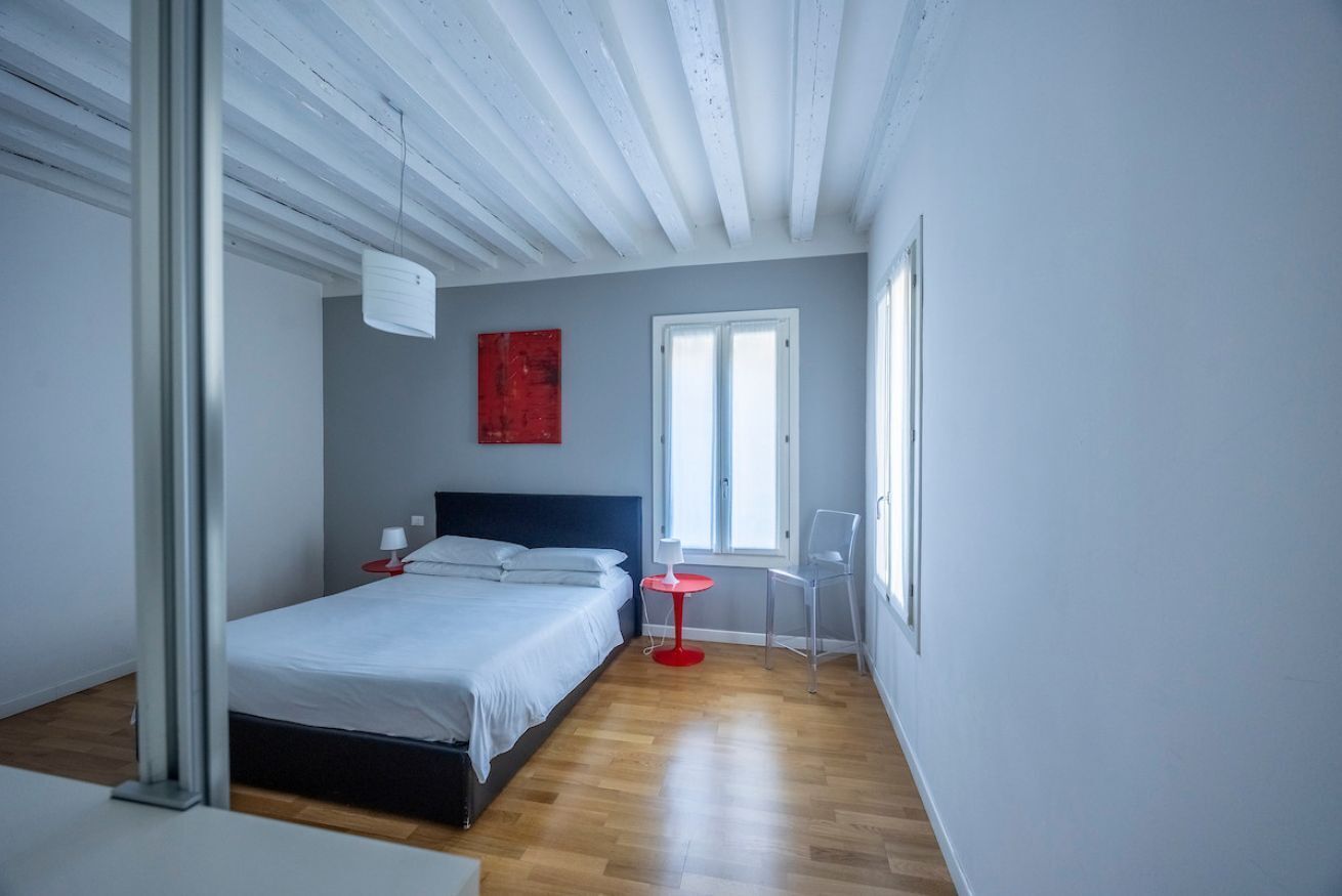 Una camera da letto con un letto, un comodino, una sedia e una finestra.