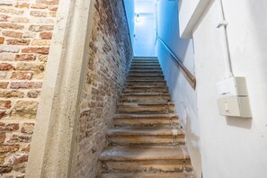 A narrow stairway with a brick wall on one side and a white wall on the other, leading to a door at the top. - Rialto al Manganer, apartment near Rialto Mercato (Venezia)