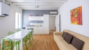 A modern kitchen with white cabinets, a dining table with green chairs, a beige sofa, and a colorful abstract painting on the wall. - Rialto al Manganer, apartment near Rialto Mercato (Venezia)