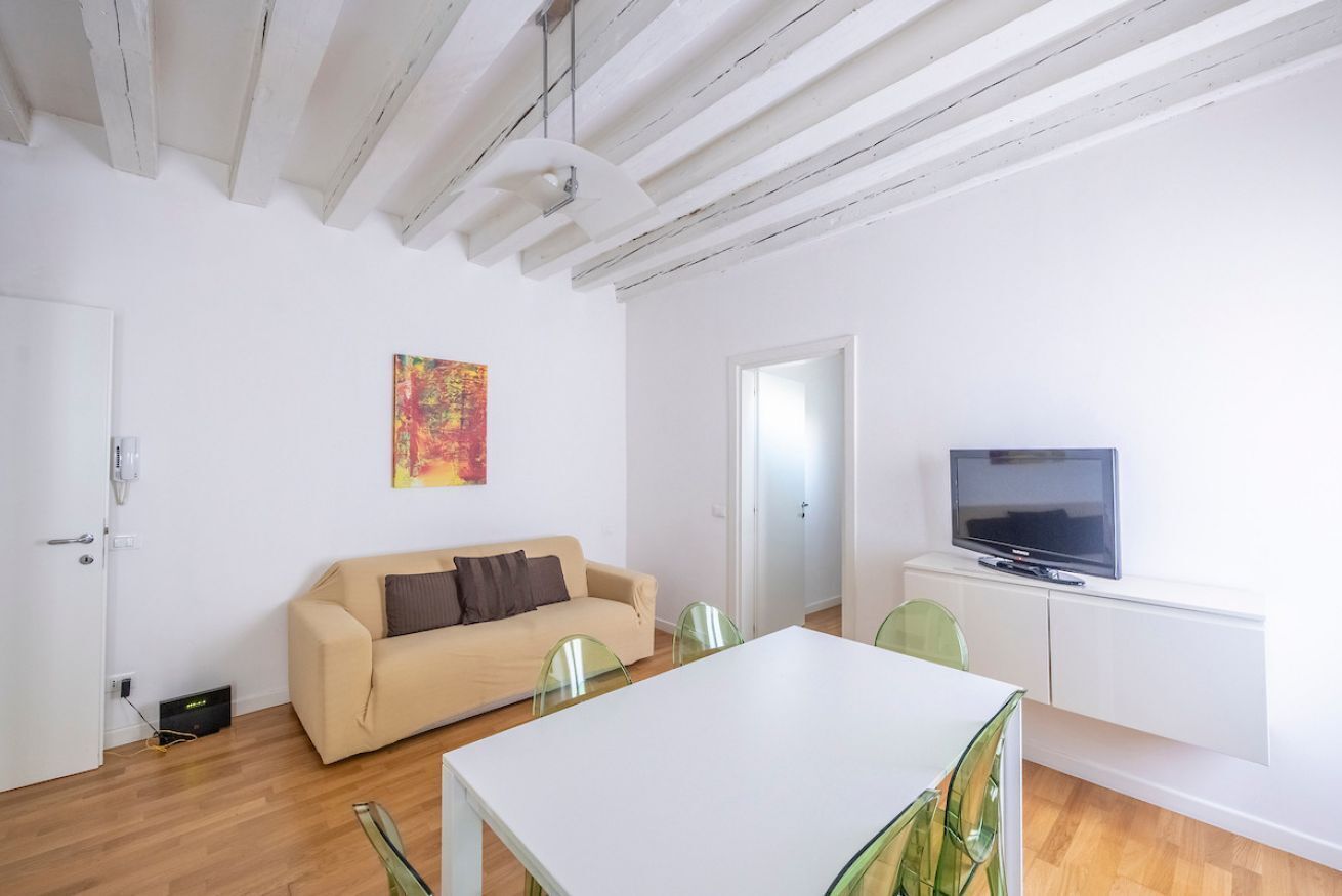 Un soggiorno moderno con un divano, un tavolo da pranzo, sedie, una televisione e un quadro appeso al muro.