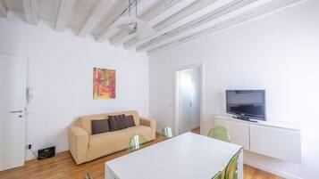 Un soggiorno moderno con un divano, un tavolo da pranzo, sedie, una televisione e un quadro appeso al muro.