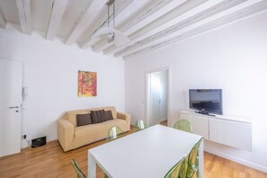 Een moderne woonkamer met een bank, een eettafel, stoelen, een televisie en een schilderij aan de muur.