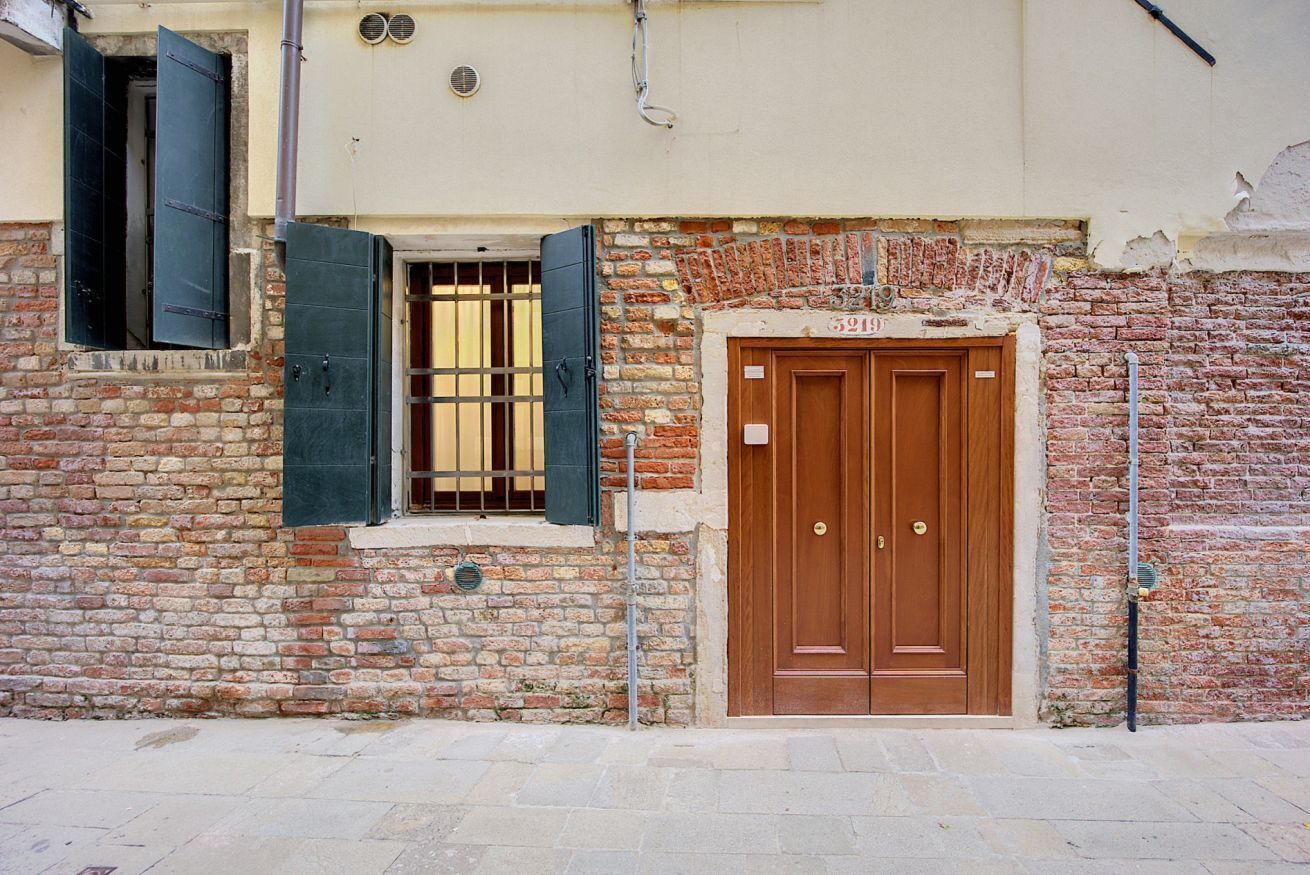 Ein Backsteinhaus mit einer hölzernen Doppeltür und einem Fenster mit grünen Fensterläden.