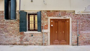 Un edificio de ladrillo con una puerta doble de madera y un ventanal con contraventanas verdes.
