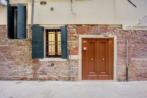 Un edificio de ladrillo con una puerta doble de madera y un ventanal con contraventanas verdes.