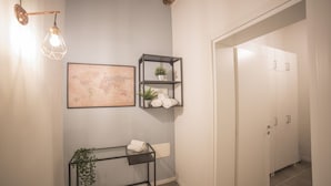Un pasillo con un mapa en la pared, una mesita consola metálica con una planta y un armario blanco.