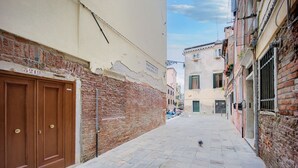Una calle estrecha con un muro de ladrillo a la izquierda y un edificio con el letrero '5919' a la derecha.