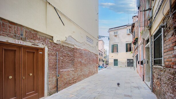 A narrow street with a brick wall on the left and a building with a sign "5919" on the right.