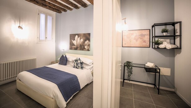Un dormitorio con cama, radiador, ventana y pared decorada con un cuadro y una repisa con toallas.