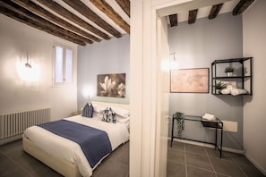 A bedroom with a bed, a radiator, a window, and a wall with a painting and a shelf with towels.