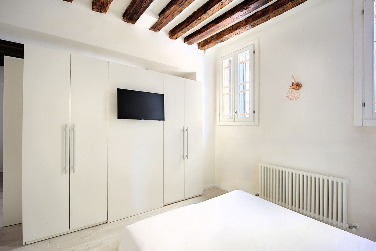 Une chambre à coucher comprenant un lit, une armoire, un téléviseur, une fenêtre et un radiateur.
