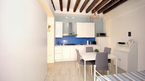 A compact kitchen with white cabinets, a blue backsplash, and a dining area with a white table and chairs.
