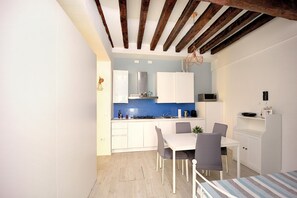 Une cuisine compacte avec des meubles blancs, un pare-feu bleu et un coin repas comprenant une table et des chaises blanches.